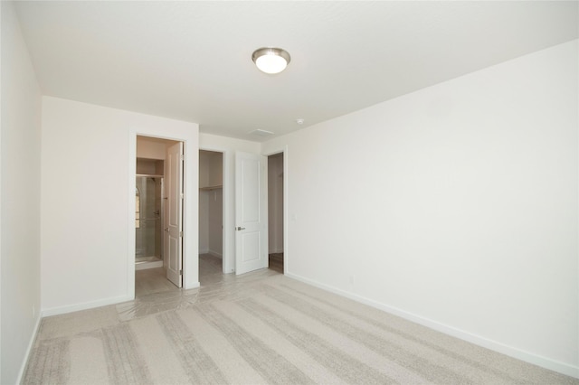 unfurnished bedroom with a walk in closet, ensuite bathroom, a closet, and light colored carpet