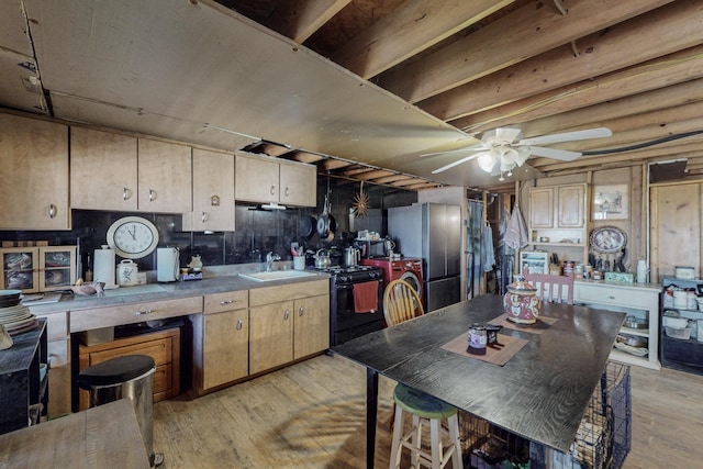 kitchen featuring sink, light wood-type flooring, stainless steel refrigerator, black gas range oven, and ceiling fan