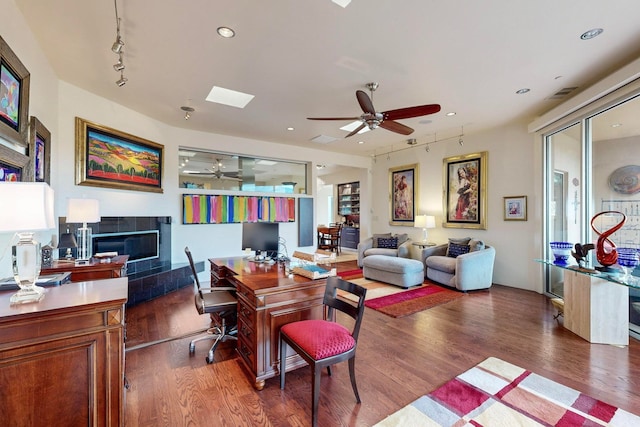 office area featuring a tiled fireplace, dark wood-type flooring, and ceiling fan