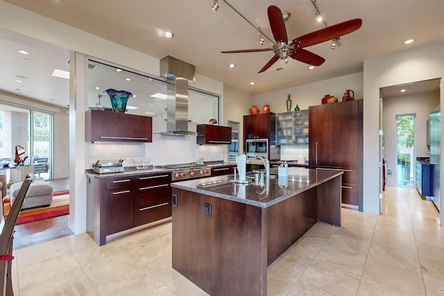 kitchen featuring tasteful backsplash, wall chimney range hood, a spacious island, stainless steel appliances, and dark stone countertops