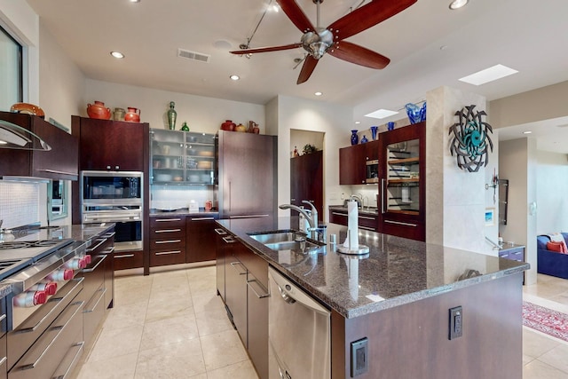 kitchen featuring an island with sink, dark stone countertops, sink, light tile patterned flooring, and appliances with stainless steel finishes