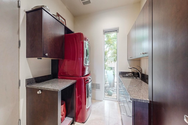 laundry room with cabinets, stacked washing maching and dryer, sink, and light tile patterned floors