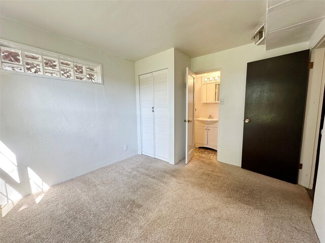 unfurnished bedroom with sink, carpet, a closet, and ensuite bath