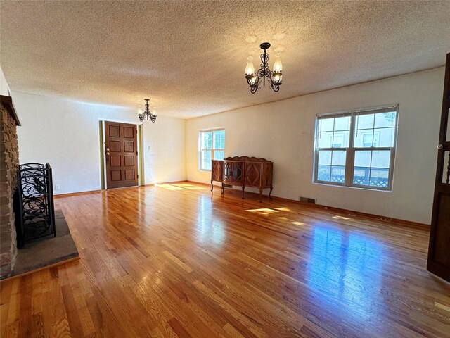 unfurnished living room featuring wood-type flooring, a textured ceiling, an inviting chandelier, and a fireplace