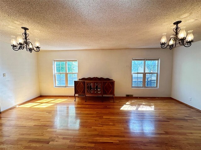 unfurnished living room featuring a textured ceiling, a notable chandelier, and hardwood / wood-style floors