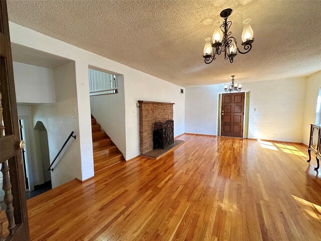 unfurnished living room with a textured ceiling, hardwood / wood-style flooring, a chandelier, and a brick fireplace