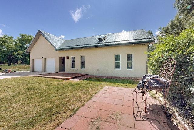 rear view of property featuring a lawn, a garage, and a patio