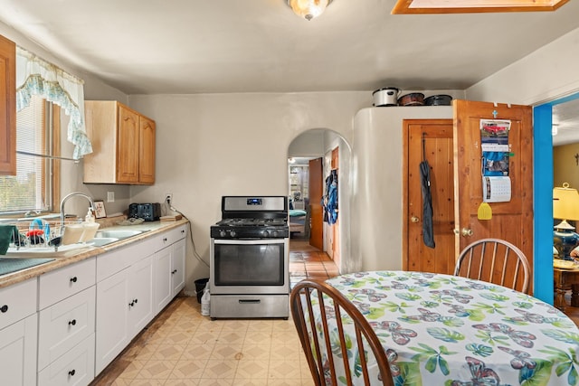 kitchen featuring arched walkways, gas range, light countertops, light floors, and a sink