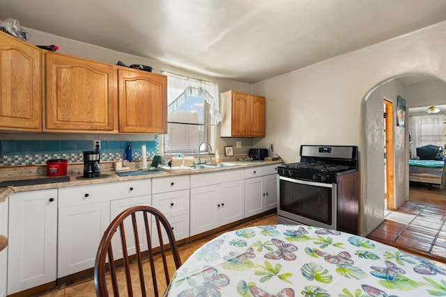 kitchen featuring arched walkways, white cabinets, gas range, backsplash, and a sink