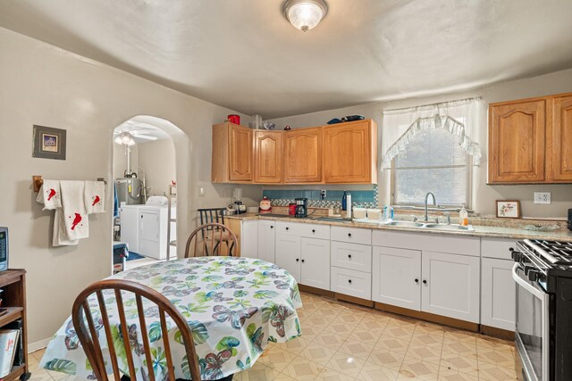 kitchen featuring arched walkways, light countertops, washing machine and dryer, stainless steel range with gas cooktop, and a sink