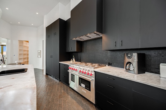 kitchen with wall chimney range hood, backsplash, dark wood-type flooring, range with two ovens, and sink