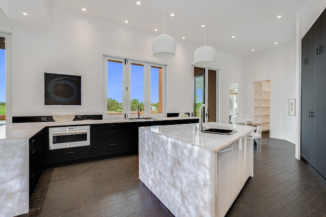 kitchen featuring sink, stainless steel oven, hanging light fixtures, and white cabinetry