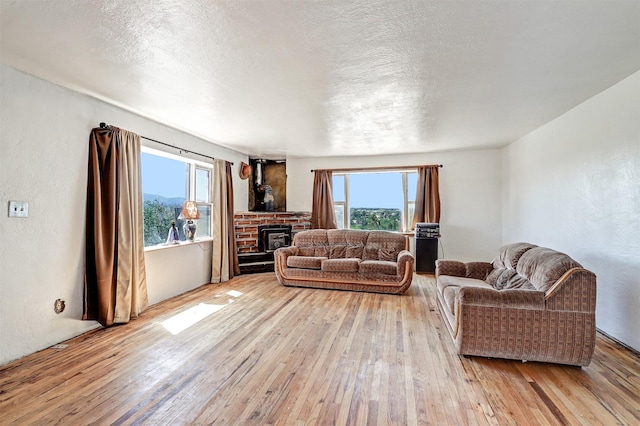 living room with a brick fireplace, a wealth of natural light, a textured ceiling, and light hardwood / wood-style floors