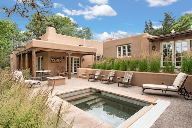 rear view of property with a swimming pool with hot tub and a patio