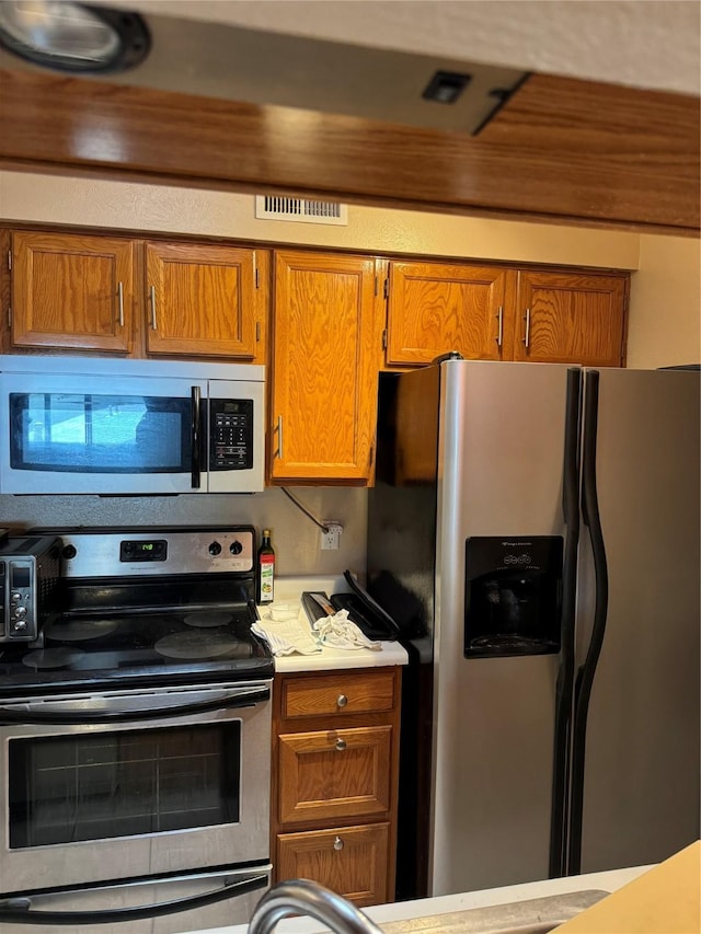 kitchen featuring light countertops, appliances with stainless steel finishes, brown cabinetry, and visible vents