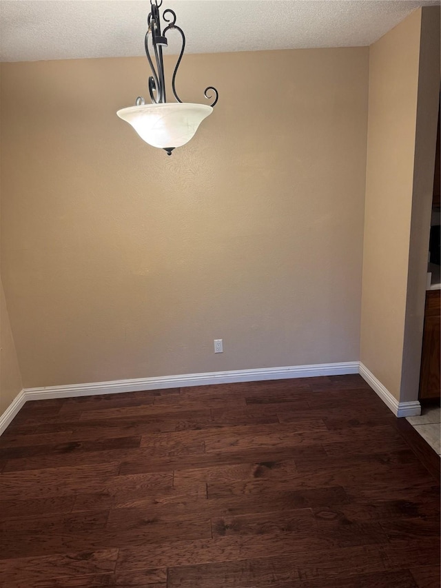 unfurnished dining area featuring dark wood-style floors, a textured ceiling, and baseboards