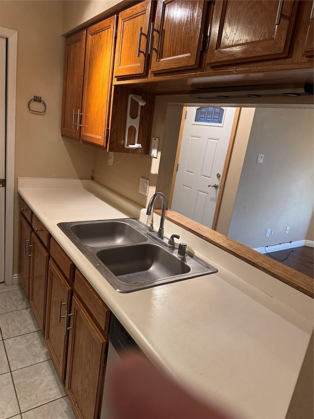 kitchen featuring light tile patterned flooring, a sink, baseboards, light countertops, and brown cabinets