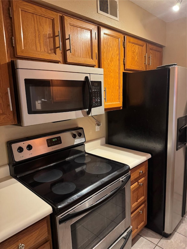 kitchen with light tile patterned floors, stainless steel appliances, visible vents, light countertops, and brown cabinets