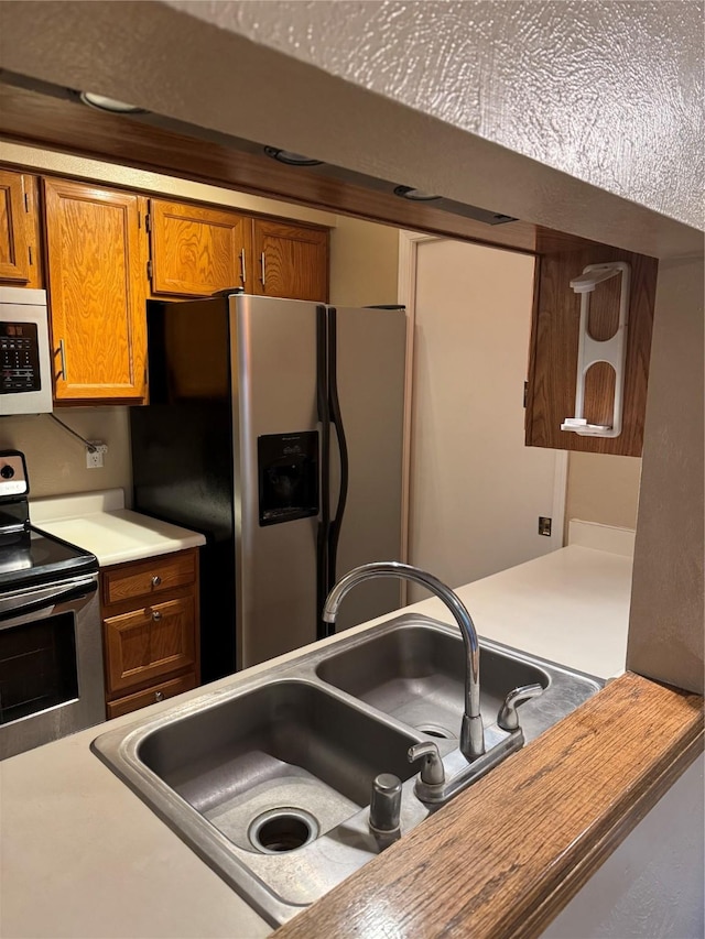 kitchen with stainless steel appliances, light countertops, brown cabinetry, and a sink