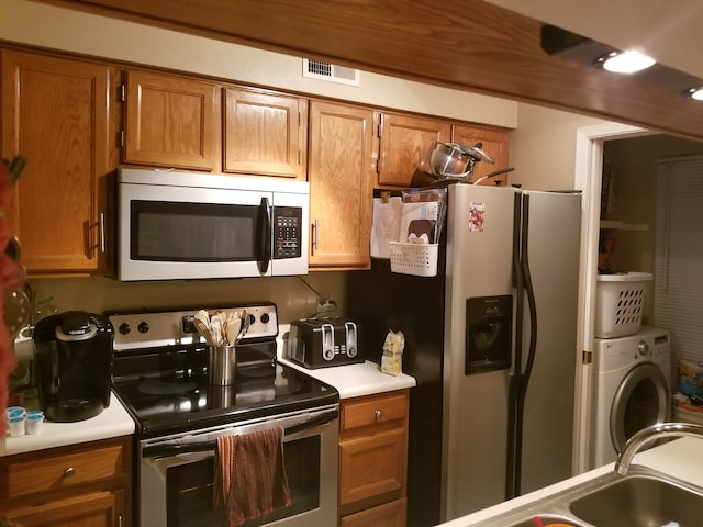 kitchen with brown cabinetry, appliances with stainless steel finishes, and washer / clothes dryer