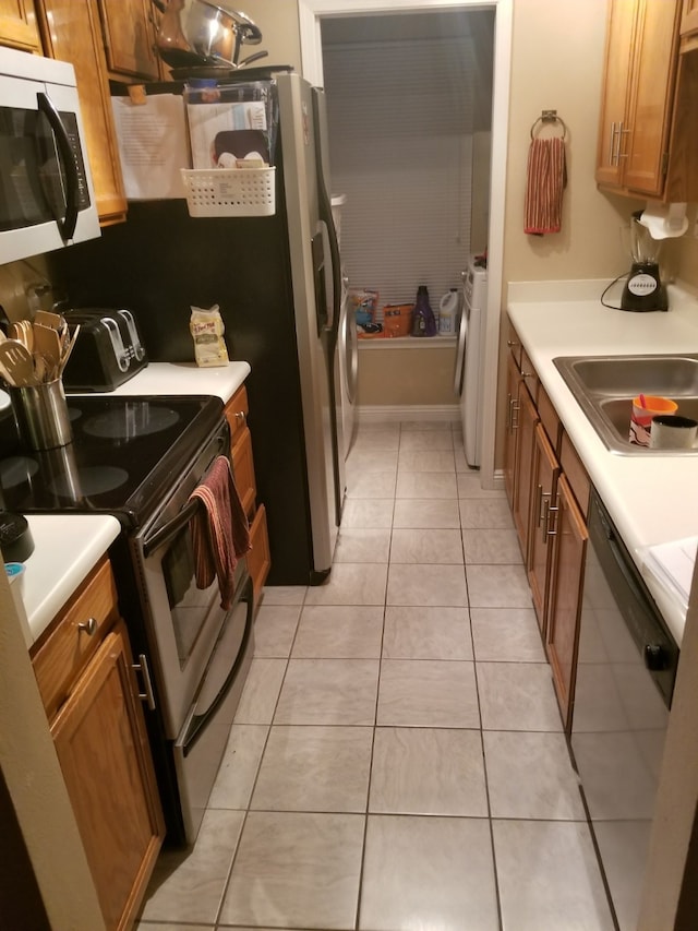 kitchen with light tile patterned floors, stainless steel appliances, brown cabinetry, and a sink