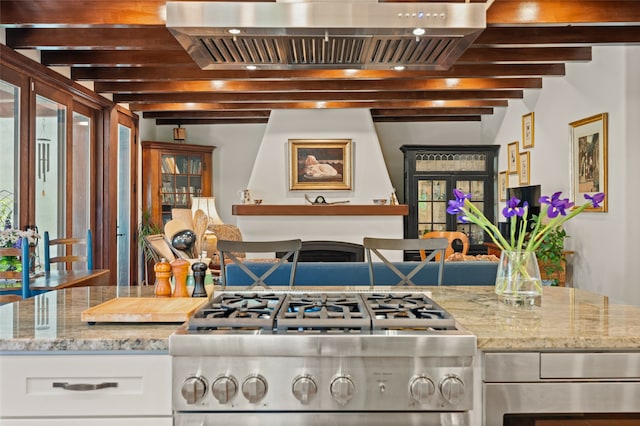 kitchen featuring range, wall chimney exhaust hood, light stone countertops, white cabinets, and beamed ceiling