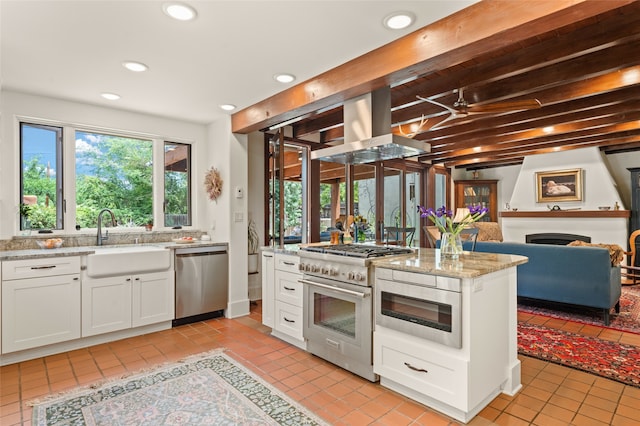 kitchen with appliances with stainless steel finishes, white cabinetry, sink, island exhaust hood, and light stone countertops