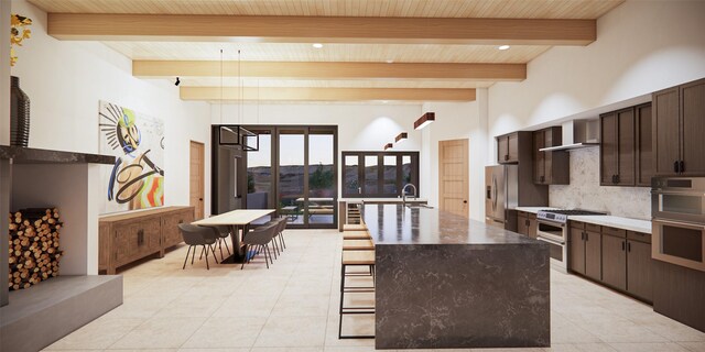 kitchen with wall chimney range hood, an island with sink, beamed ceiling, a breakfast bar, and backsplash