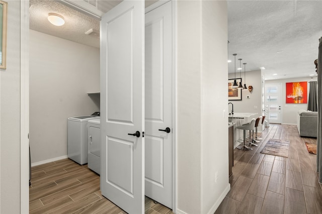 clothes washing area with sink, wood-type flooring, a textured ceiling, and independent washer and dryer