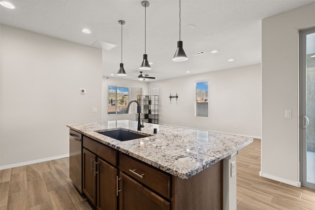 kitchen featuring light stone counters, stainless steel dishwasher, sink, a center island with sink, and light hardwood / wood-style flooring