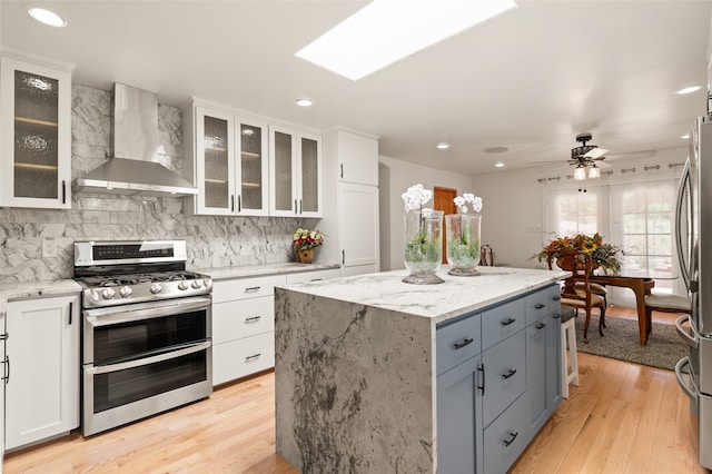 kitchen featuring a kitchen island, white cabinetry, light stone countertops, stainless steel appliances, and wall chimney exhaust hood