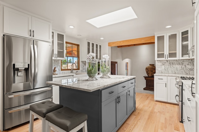 kitchen featuring a skylight, white cabinetry, appliances with stainless steel finishes, a kitchen island, and light stone counters