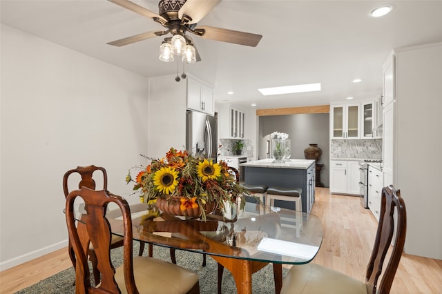 dining area featuring ceiling fan, a skylight, and light hardwood / wood-style floors