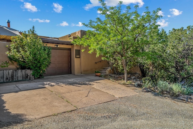 view of front facade with a garage, concrete driveway, fence, and stucco siding