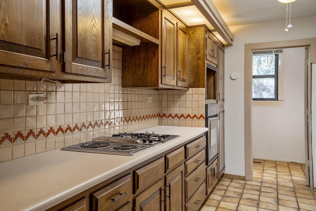 kitchen with oven, baseboards, light countertops, decorative backsplash, and stainless steel cooktop