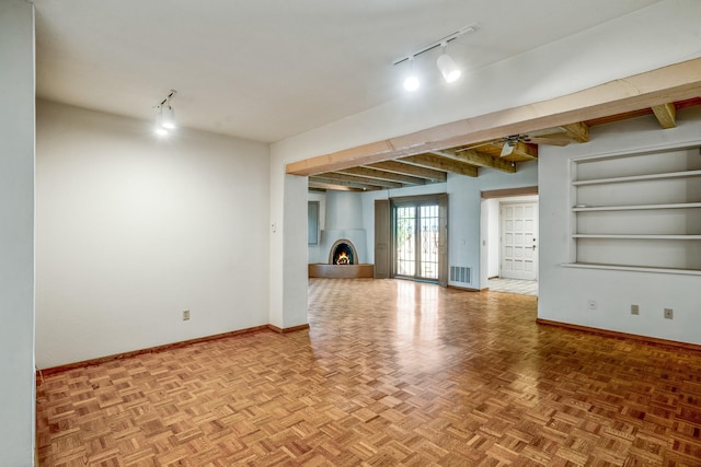 unfurnished room featuring a warm lit fireplace, visible vents, baseboards, and beam ceiling