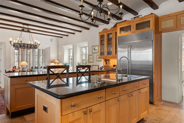 kitchen with sink, an inviting chandelier, beamed ceiling, a kitchen island with sink, and stainless steel built in fridge