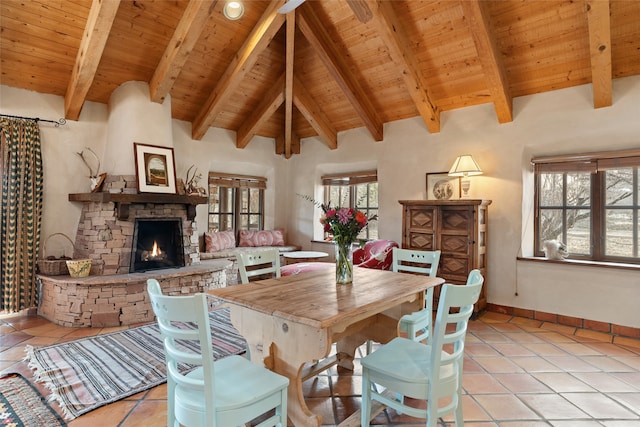 dining area with a stone fireplace, lofted ceiling with beams, light tile patterned floors, and wooden ceiling