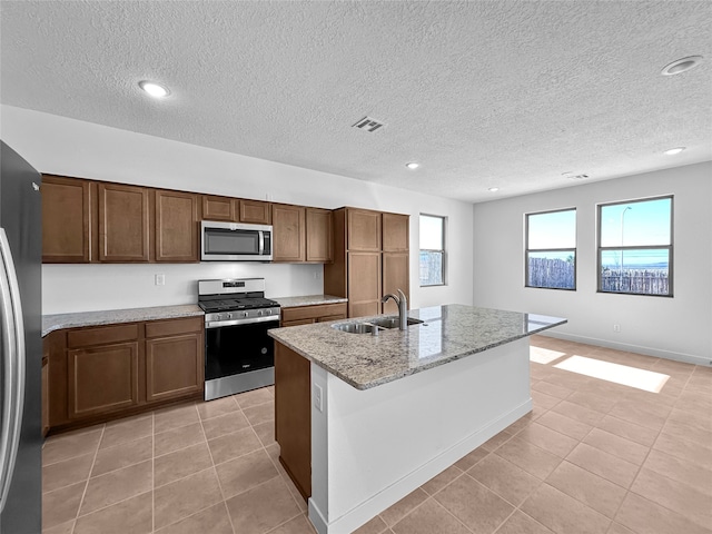 kitchen with light stone countertops, a textured ceiling, stainless steel appliances, sink, and a center island with sink