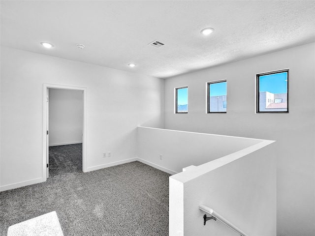 empty room with dark colored carpet, a healthy amount of sunlight, and a textured ceiling