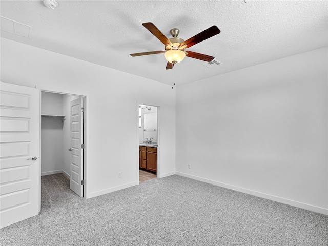 unfurnished bedroom featuring connected bathroom, ceiling fan, a textured ceiling, light carpet, and a closet