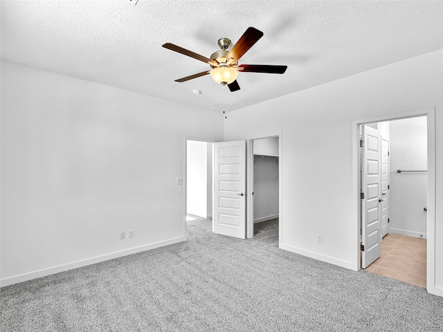 unfurnished bedroom with a walk in closet, ensuite bath, a textured ceiling, light colored carpet, and ceiling fan