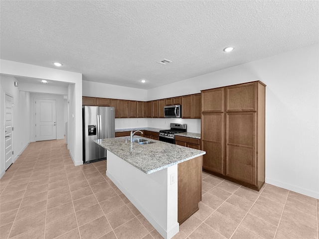 kitchen featuring sink, light stone countertops, a textured ceiling, an island with sink, and appliances with stainless steel finishes