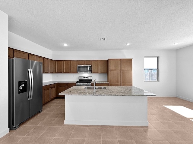 kitchen with light stone counters, sink, a kitchen island with sink, and appliances with stainless steel finishes