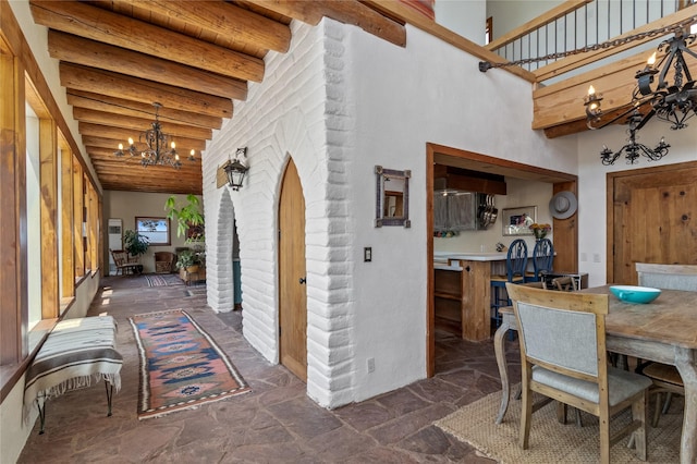 dining room featuring stone tile floors, wood ceiling, a towering ceiling, beam ceiling, and an inviting chandelier