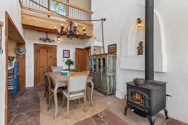 dining area featuring a wood stove, an inviting chandelier, a towering ceiling, and stone finish floor