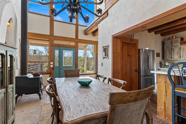 dining room featuring beam ceiling, a towering ceiling, a wood stove, and an inviting chandelier