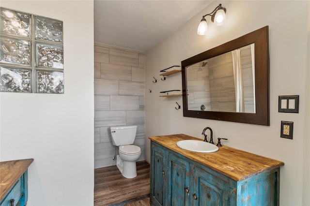 bathroom with toilet, wood finished floors, vanity, and tile walls