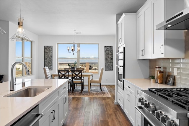 kitchen featuring sink, decorative light fixtures, wall chimney range hood, stainless steel appliances, and white cabinets