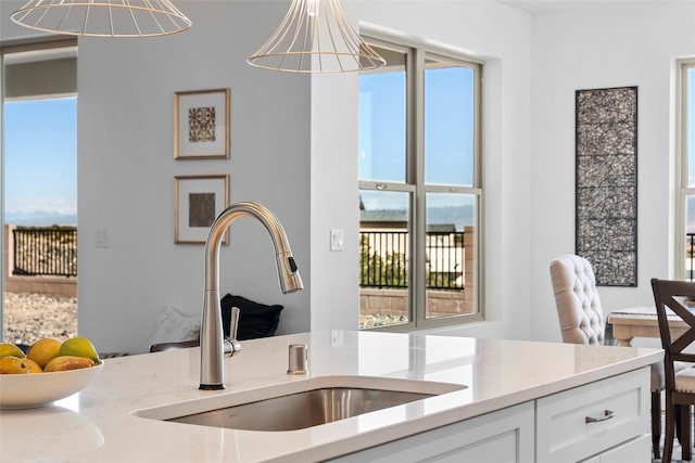 kitchen with sink, white cabinetry, an inviting chandelier, light stone counters, and hanging light fixtures